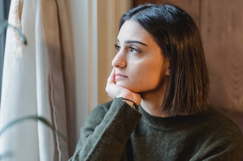 Smutna młoda kobieta wygląda przez okno