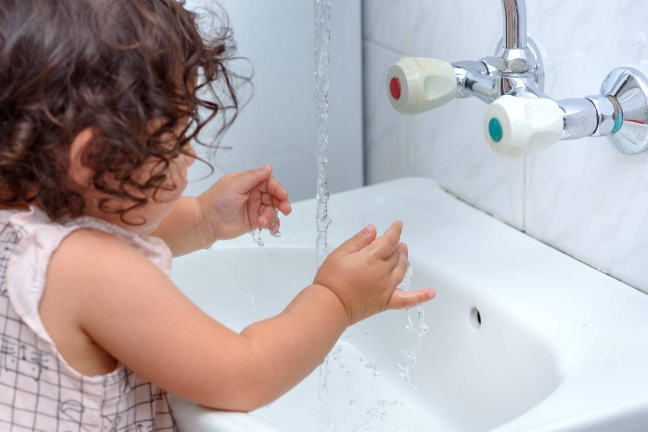 Mała dziewczynka w żłobku myje ręce przed posiłkiem.