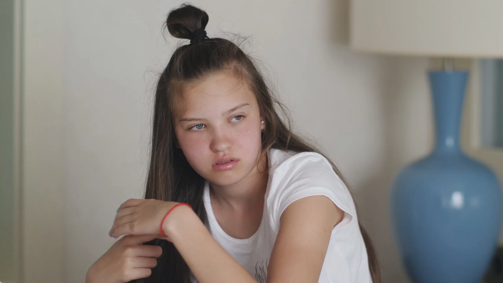 Nastoletnie dziewczynka siedzi na łóżku z naburmuszoną miną