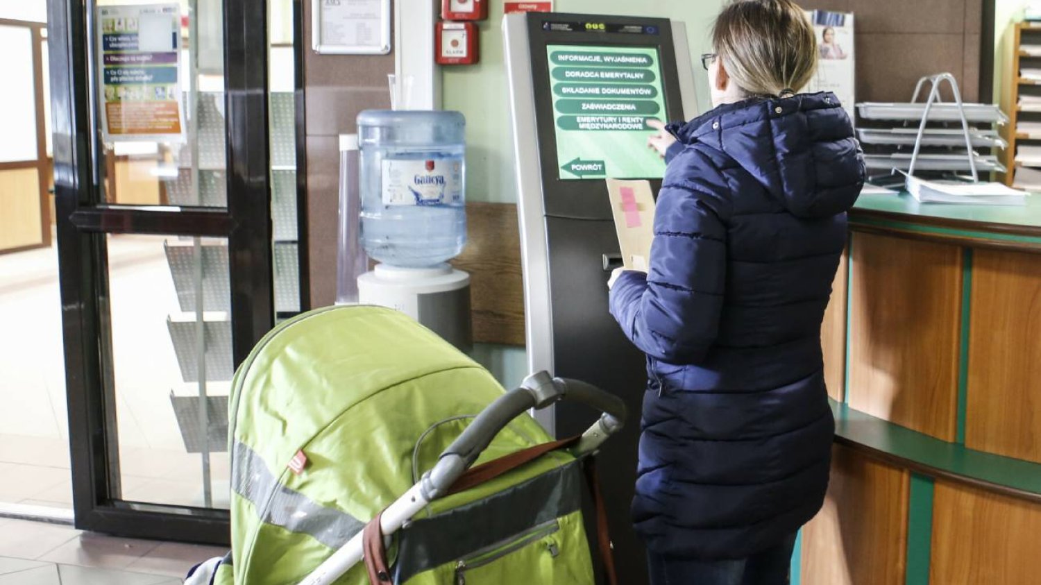 Matka z wózkiem w urzędzie, składa dokumenty o świadczenia na dziecko 2024.