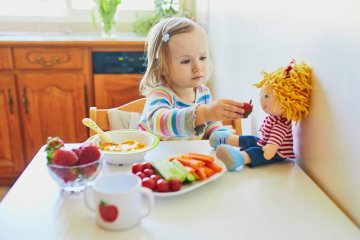Dziewczynka karmi lalkę przekąskami dla dzieci.