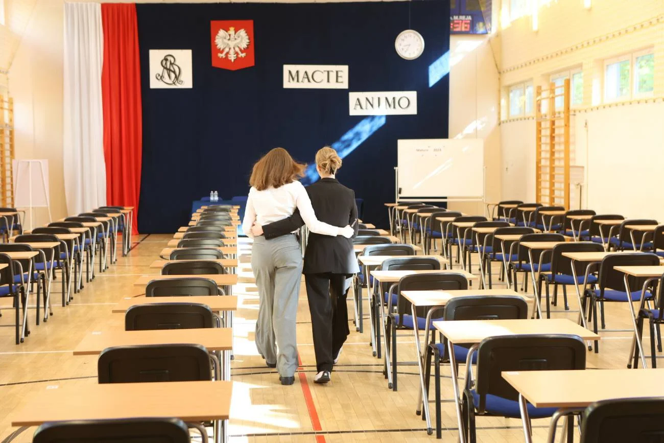 Maturzystki idą na egzamin i wspierająco się ściskają.
