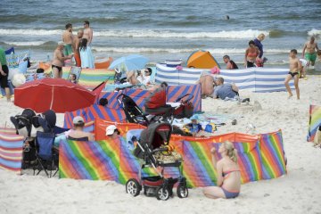 Mama pilnuje na plaży dziecka śpiącego w wózku.