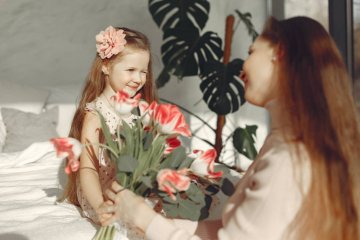 Dziewczynka składa mamie śmieszne życzenia na Dzień Mamy i daje jej kwiaty.