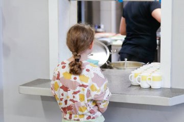 Dziecko czeka na posiłek w okienku na stołówce szkolnej.