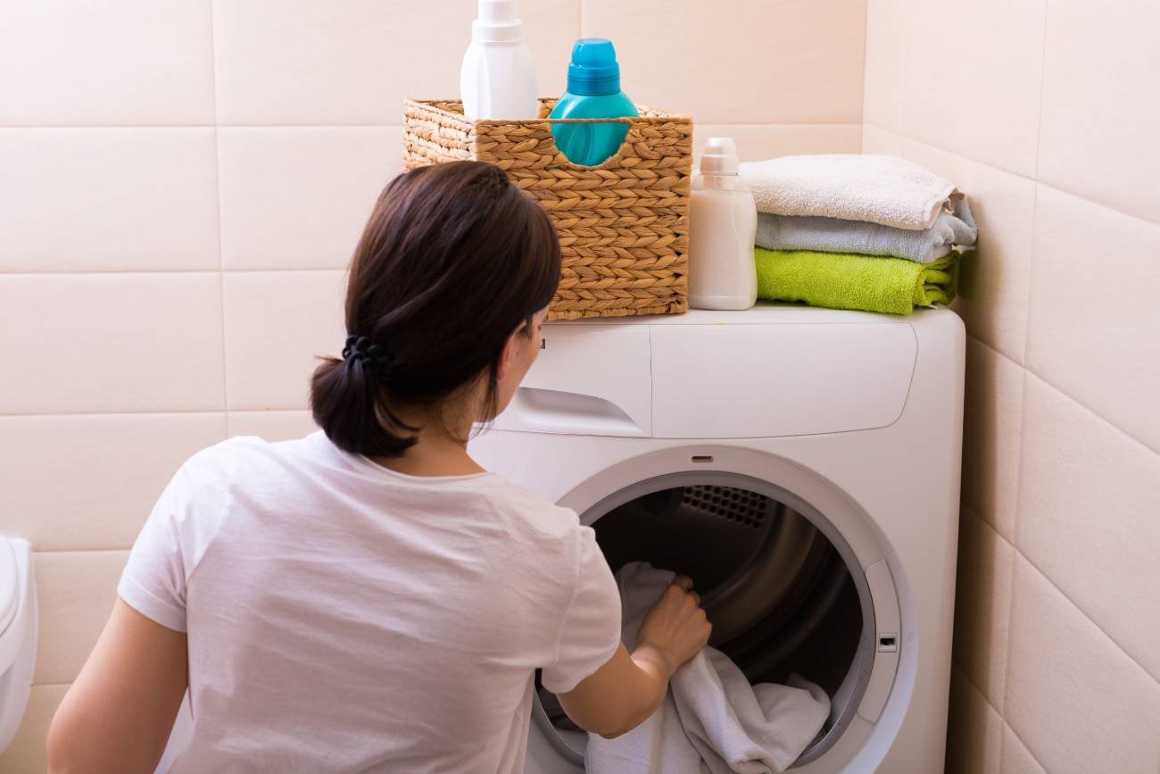 Kobieta wkładająca ubrania do pralki.