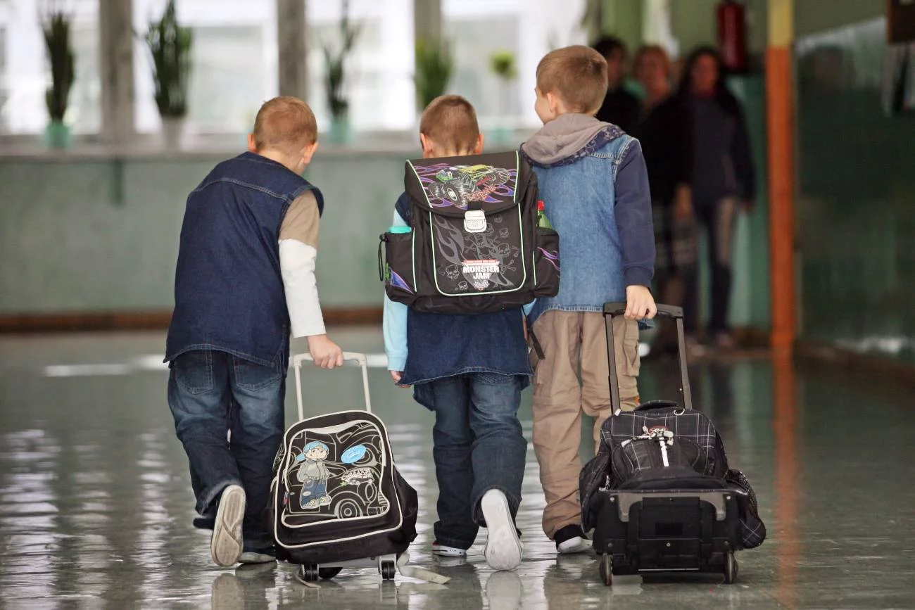 pierwszoklasiści idą szkolnym korytarzem z plecakami pierwszoklasiści idą szkolnym korytarzem z plecakami