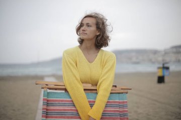 Samotna kobieta niosąca leżak i rozmyślająca na plaży.