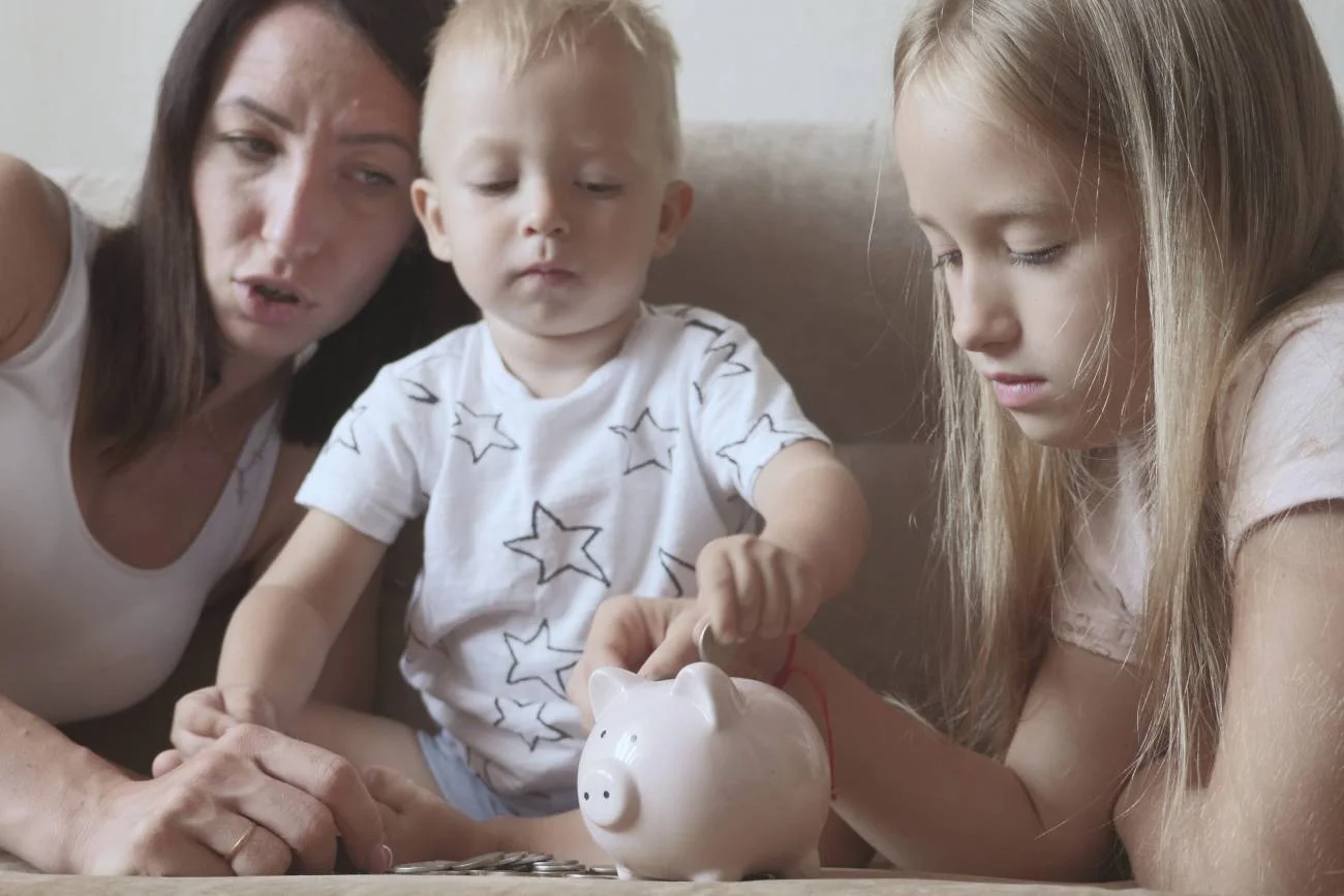 mama z dziećmi wrzuca pieniądze do skarbonki mama z dziećmi wrzuca pieniądze do skarbonki
