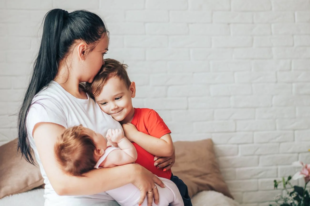 Zmęczona mama opiekuje się dwójką dzieci: małym chłopcem i noworodkiem.