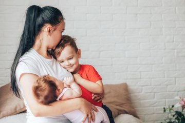 Zmęczona mama opiekuje się dwójką dzieci: małym chłopcem i noworodkiem.