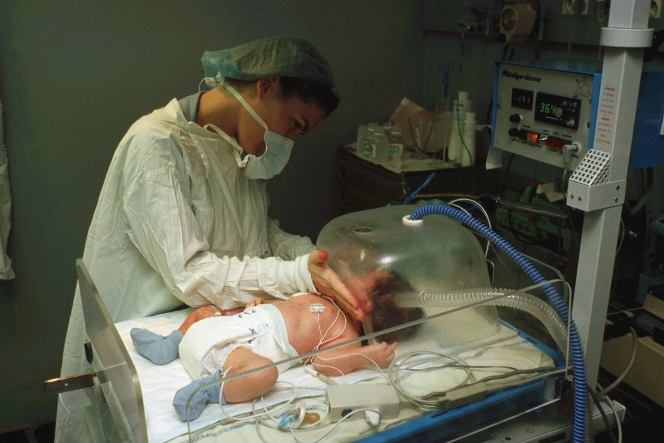 Opiekunka zajmuje się niemowlakiem w hospicjum i nosi maseczkę.