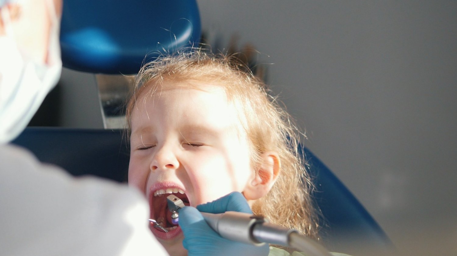 Na zdjęciu widać dziewczynkę, która siedzi u dentysty i ma robiony ząb