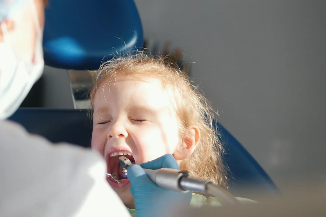 Na zdjęciu widać dziewczynkę, która siedzi u dentysty i ma robiony ząb