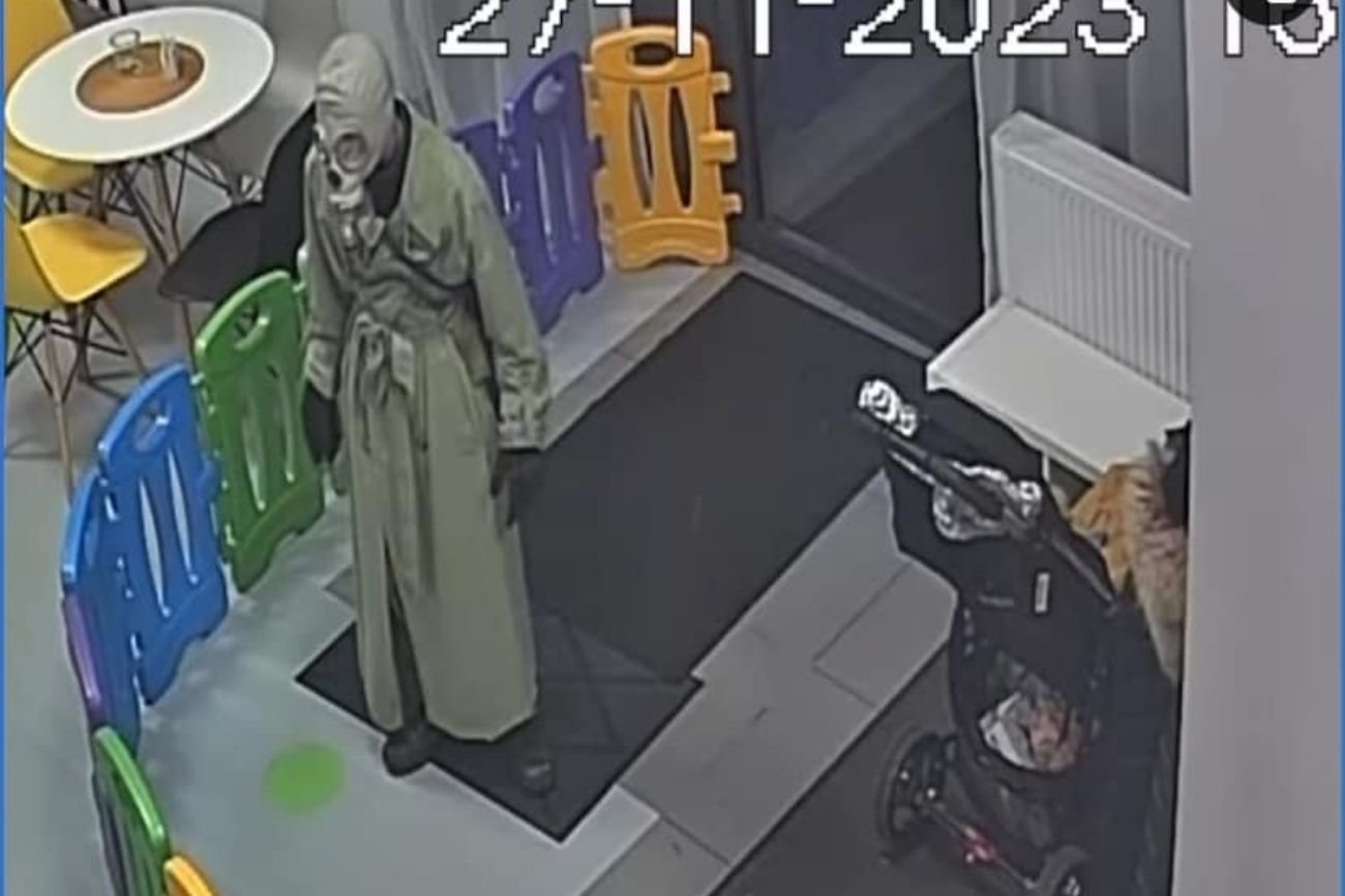 Postać w masce przeciwgazowej i płaszczu na zdjęciu z monitoringu sali zabaw.