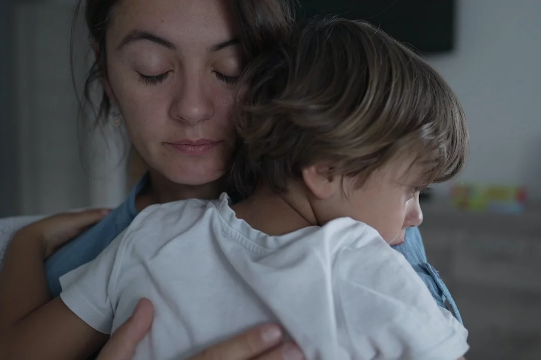 Na zdjęciu widać kobietę z zamkniętymi oczami, która przytula swoje dziecko