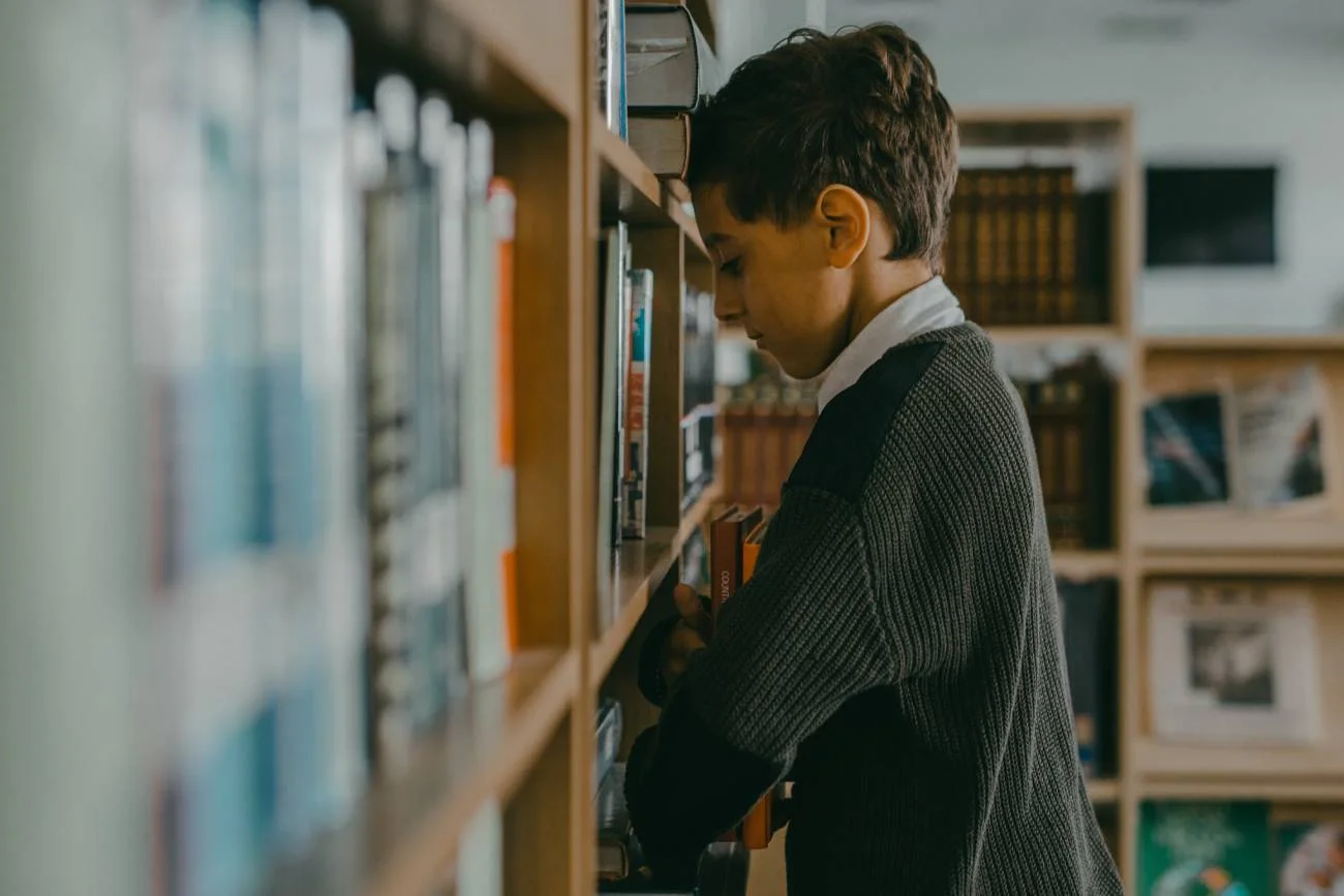 Smutny chłopiec w szkolnej bibliotece opiera czoło o książki.