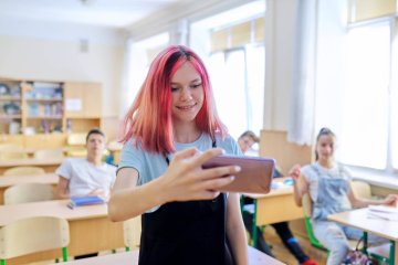 Uczennica szkoły średniej stoi w klasie z telefonem i robi selfie. Uczennica szkoły średniej robi sobie telefonem selfie.