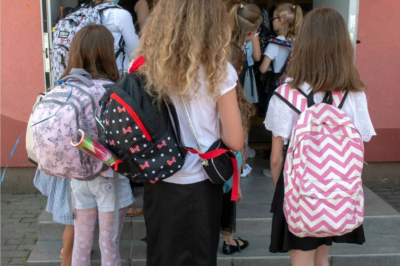 Dzieci z plecakami wchodzą do budynku szkoły.