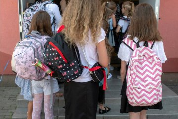 Dzieci z plecakami wchodzą do budynku szkoły.