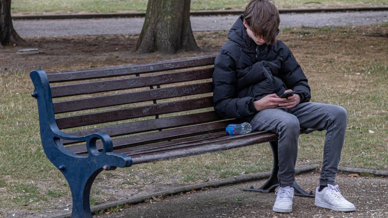 Nastolatek siedzi na ławce w parku ze smartfonem w dłoniach. Nastolatek siedzi na ławce w parku ze smartfonem w dłoniach.