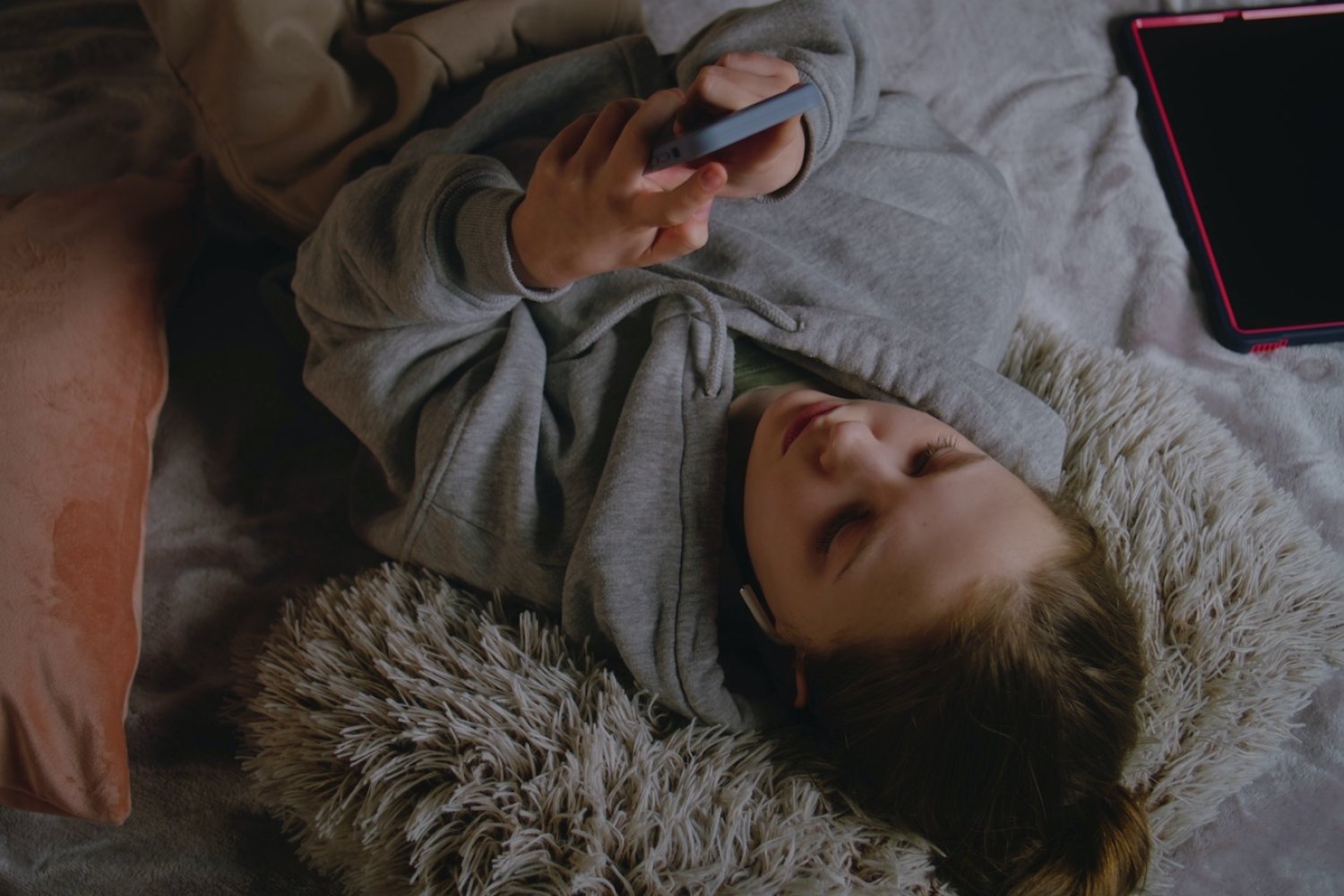 Na zdjęciu nastolatka leży na łóżku i patrzy w telefon.