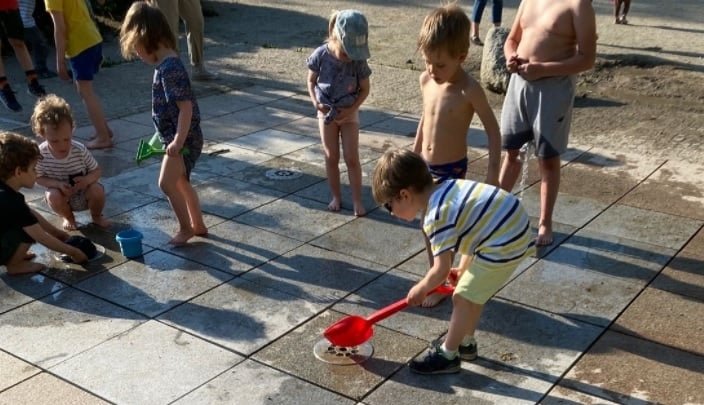 Dzieci bawią się w fontannie i wsypują piasek do dysz.