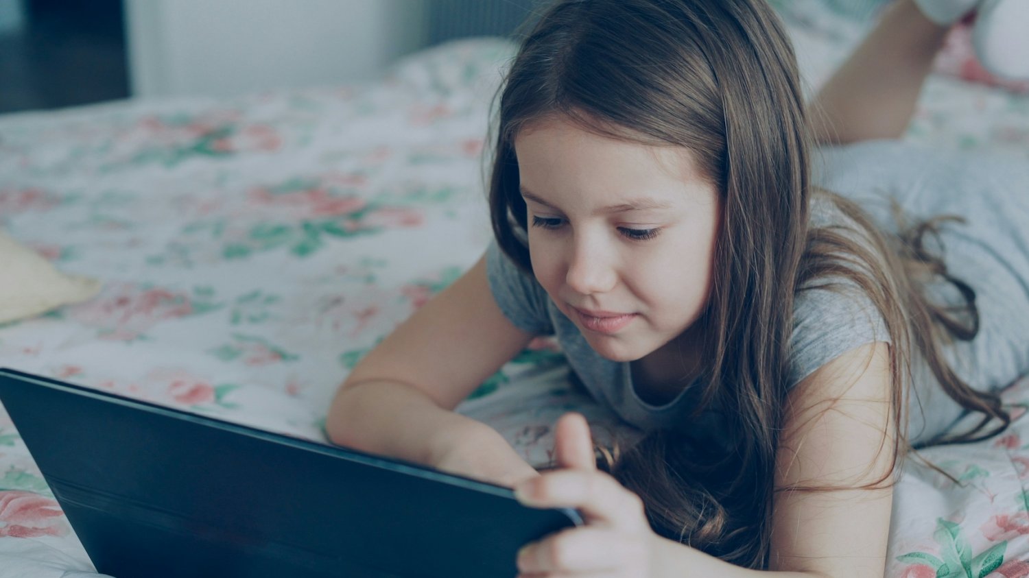 Gigantyczne odszkodowanie za wpływ social mediów. Zaczęła w wieku 6 lat Na zdjęciu dziewczynka leży z tabletem na łóżku.