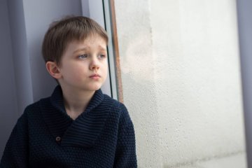 Mały chłopiec wygląda zmartwiony przez okno.