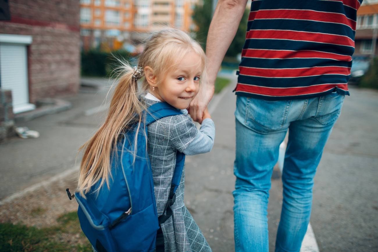 Dziewczynka idzie z plecakiem i opiekunem do szkoły.