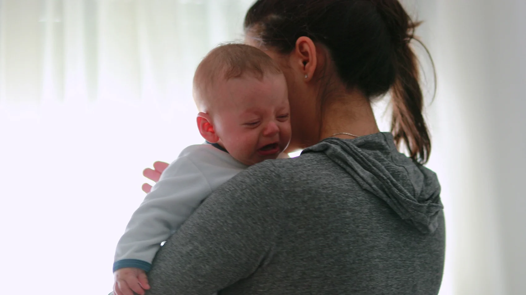 Syndrom oszusta dotyka także matki – na czym polega to zjawisko? Na zdjęciu mama trzyma płaczące dziecko – nie widać jej twarzy (bo jest odwrócona)