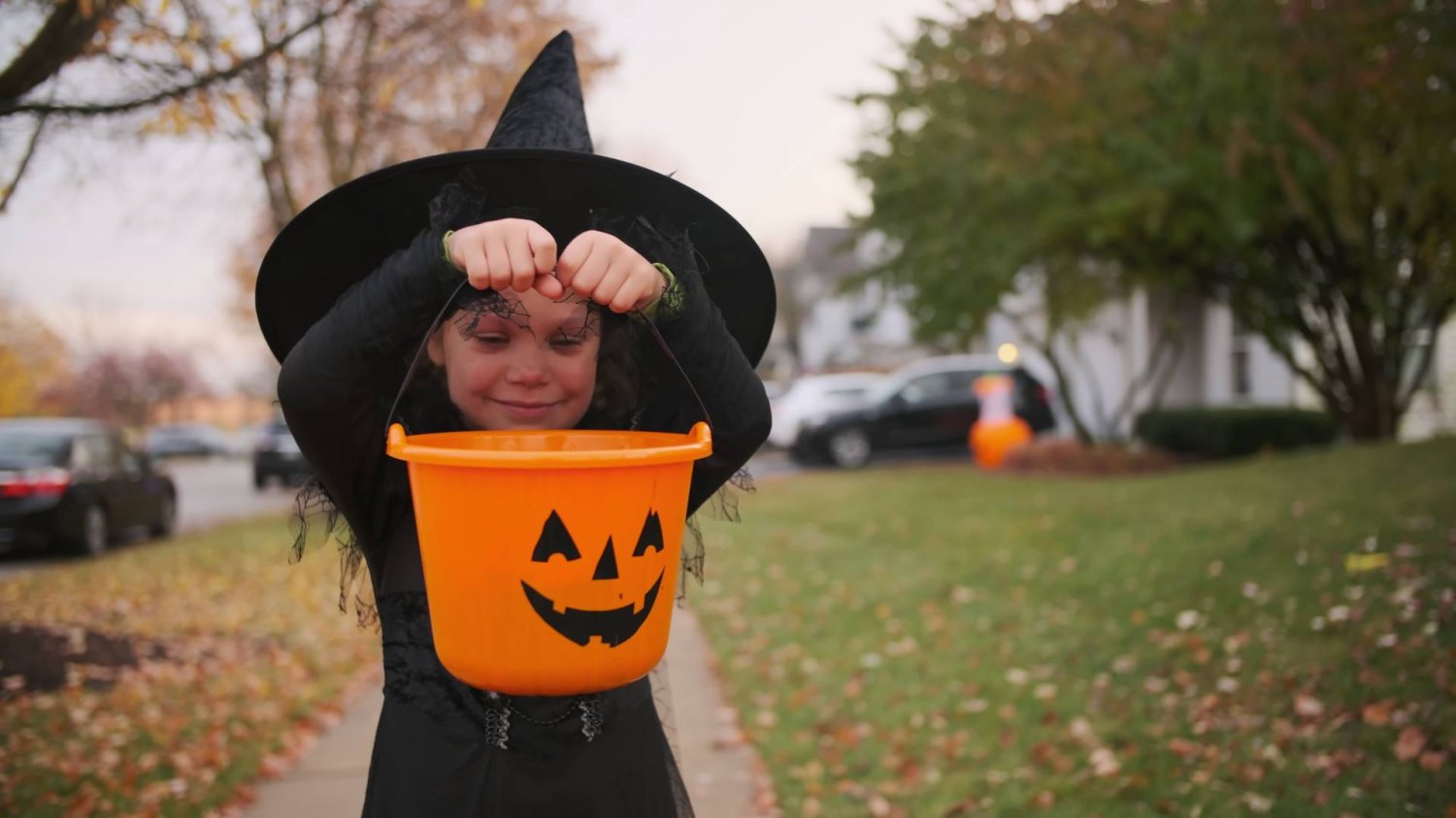 Dziewczynka przebrana na Halloween za wiedźmę z wiaderkiem na słodycze