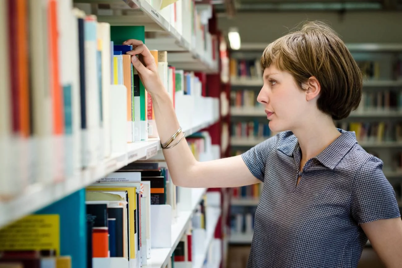 Szkolna bibliotekarka przed regałem książek. Szkolna bibliotekarka przed regałem książek.
