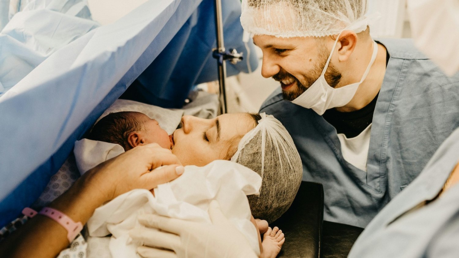 Czego można się spodziewać podczas porodu? Na zdjęciu widać sytuację zaraz po porodzie - mama przytula noworodka. Tata stoi za nimi.