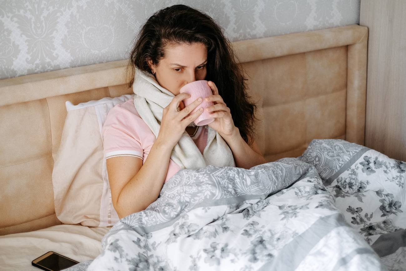 Przeziębiona kobieta leży w łóżku i pije herbatę z głogiem.