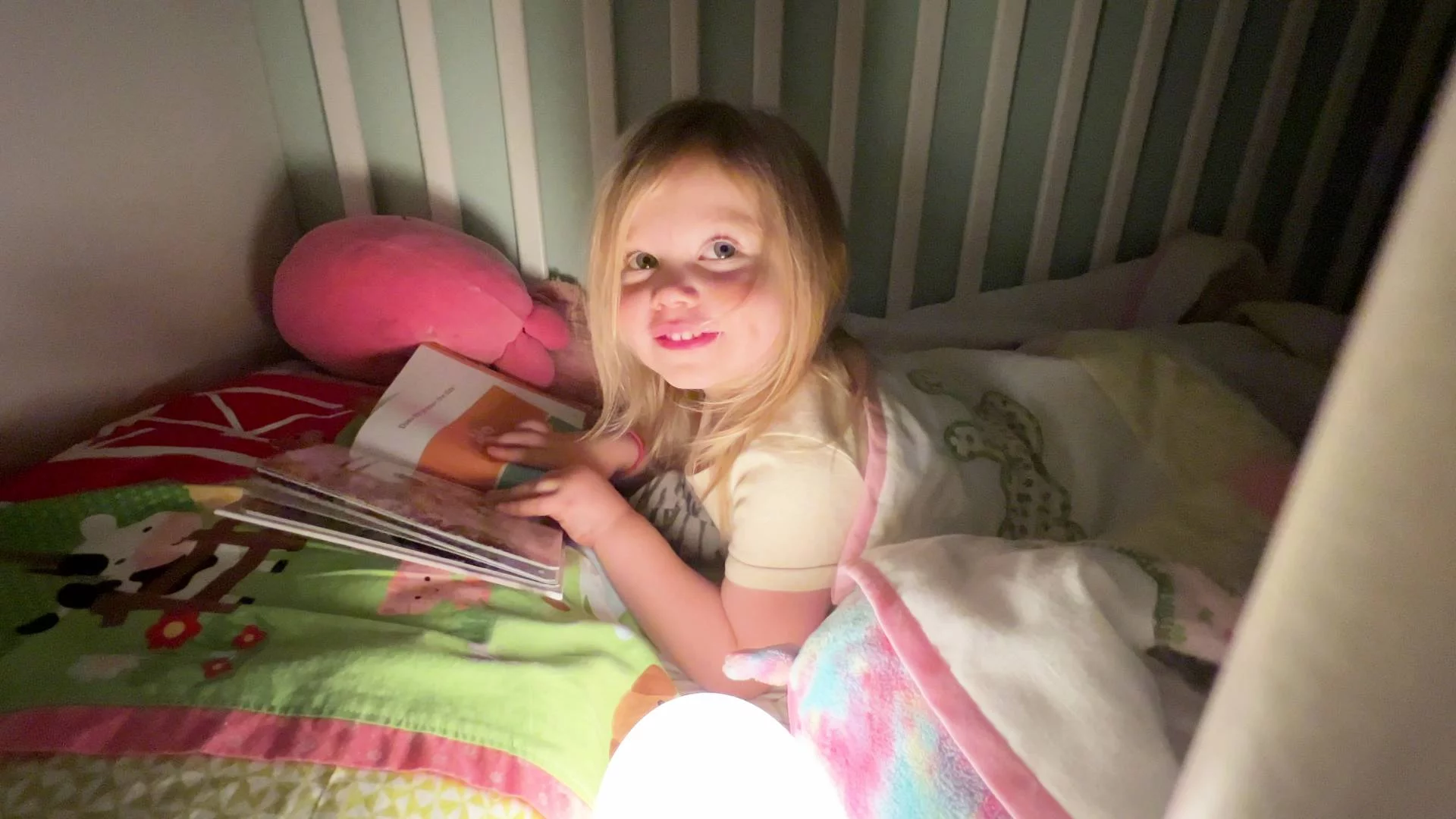 Mała dziewczynka leży w łóżku i ogląda obrazki w książce