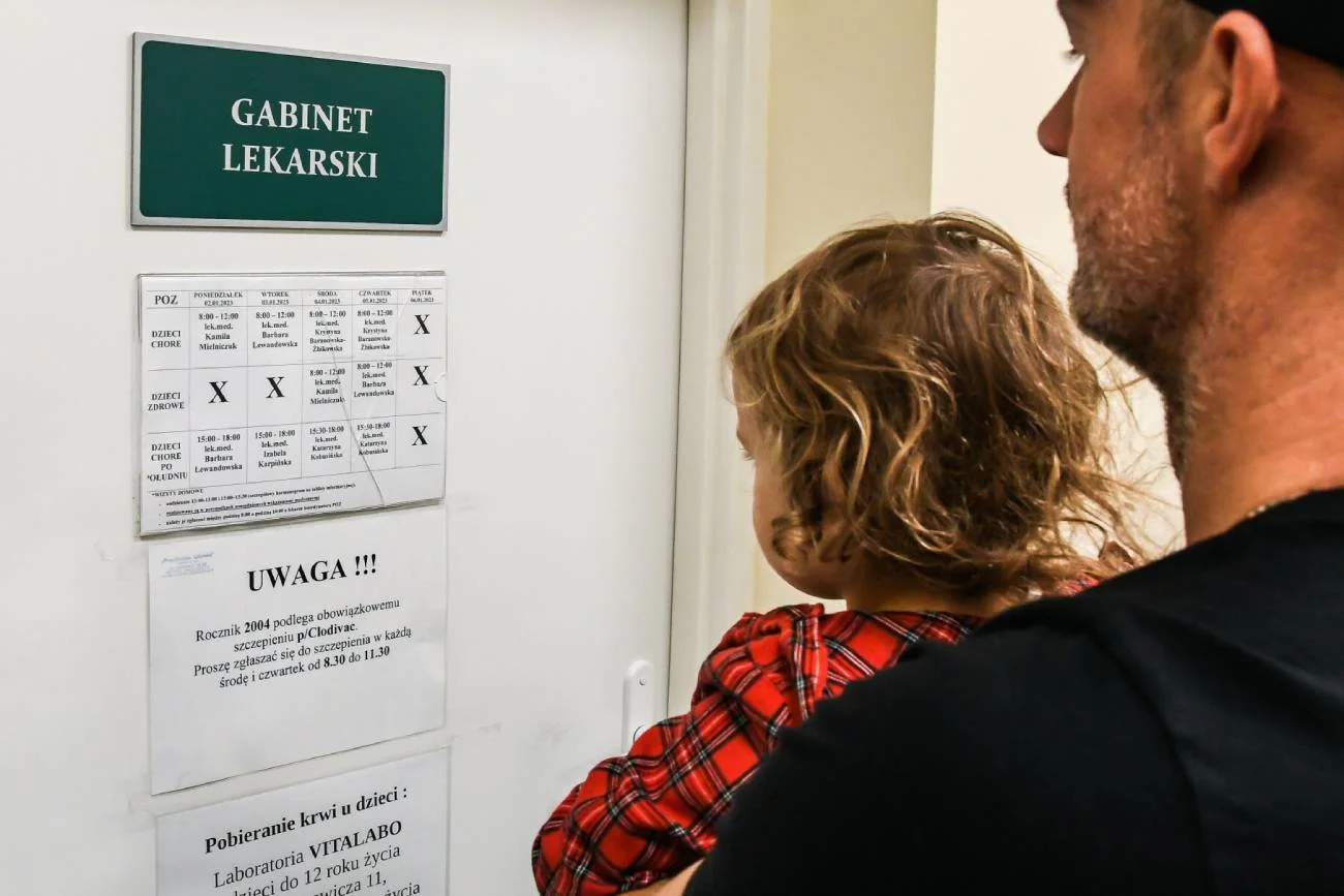 Rodzic z dzieckiem przed wejściem do gabinetu lekarskiego, gdzie wykonuje się szczepienie przeciwko odrze.