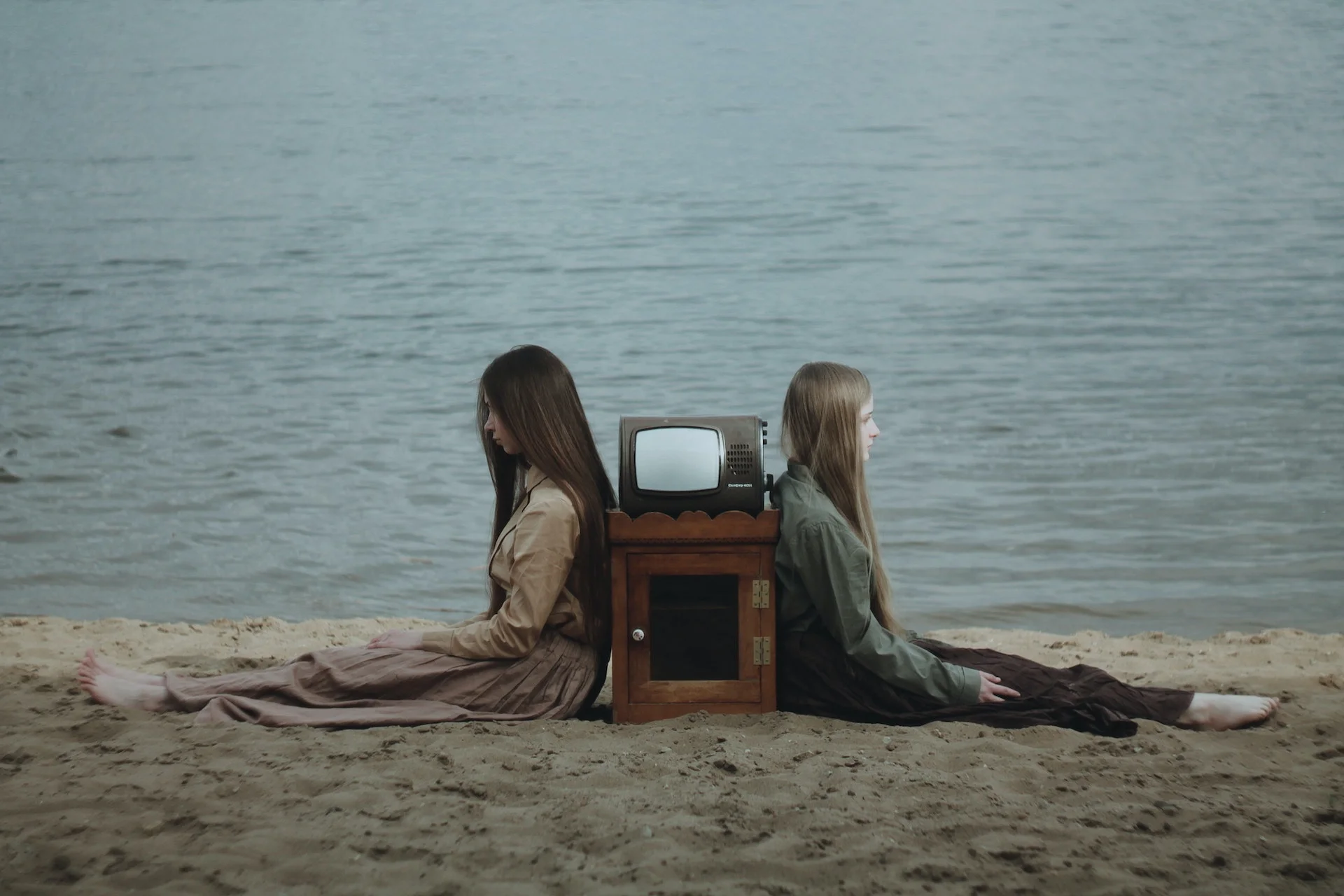 Nastolatki siedzą na plaży, między nimi stoi stary telewizor.