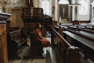 Wnętrze kościoła, na ławce siedzi młoda kobieta w sukience.