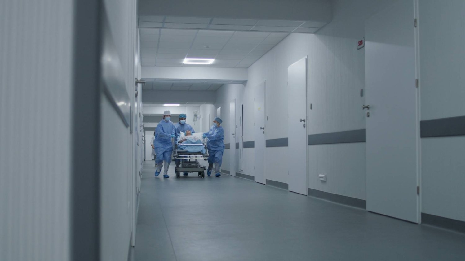 lekarze biegną z pacjentem na łóżku przez korytarz szpitala