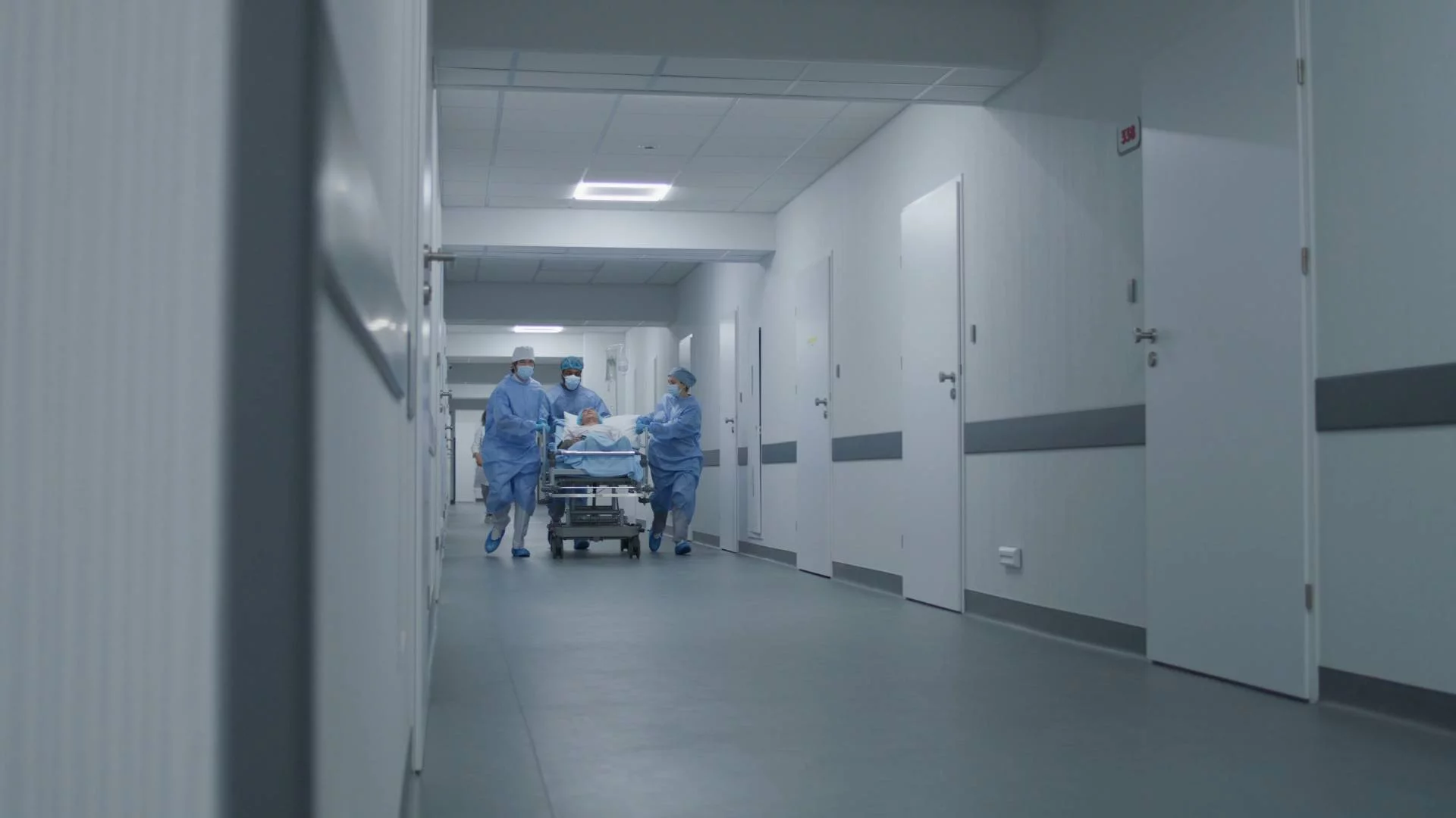 lekarze biegną z pacjentem na łóżku przez korytarz szpitala