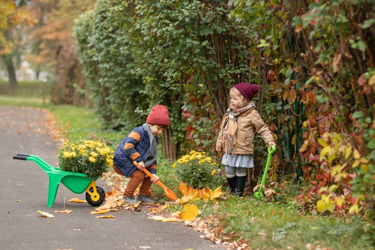 Dwoje dzieci sprząta ogród i grabi liście.