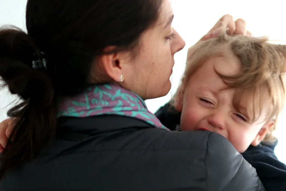 Dzieci przed wejściem do przedszkola często odczuwają dyskomfort i płaczą Na zdjęciu widać płaczące dziecko, które mama trzyma na rękach