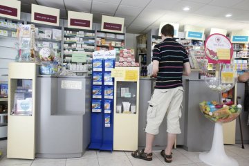 Młody mężczyzna stoi przy ladzie w aptece i kupuje syrop przeciwbólowy.