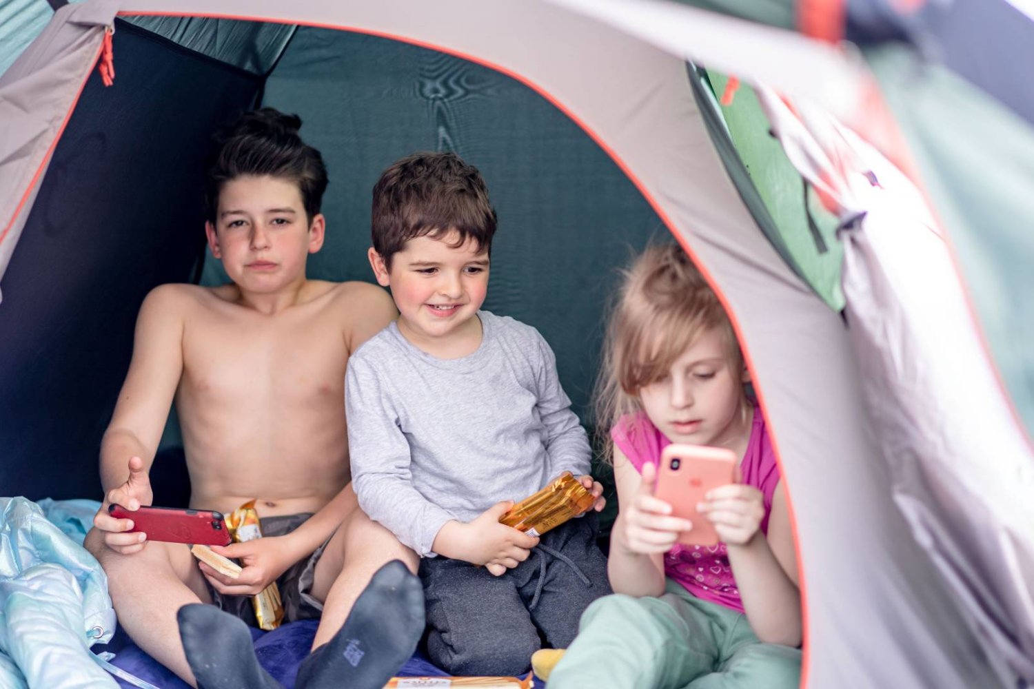 dzieci w namiocie patrzą w ekrany smartfonów