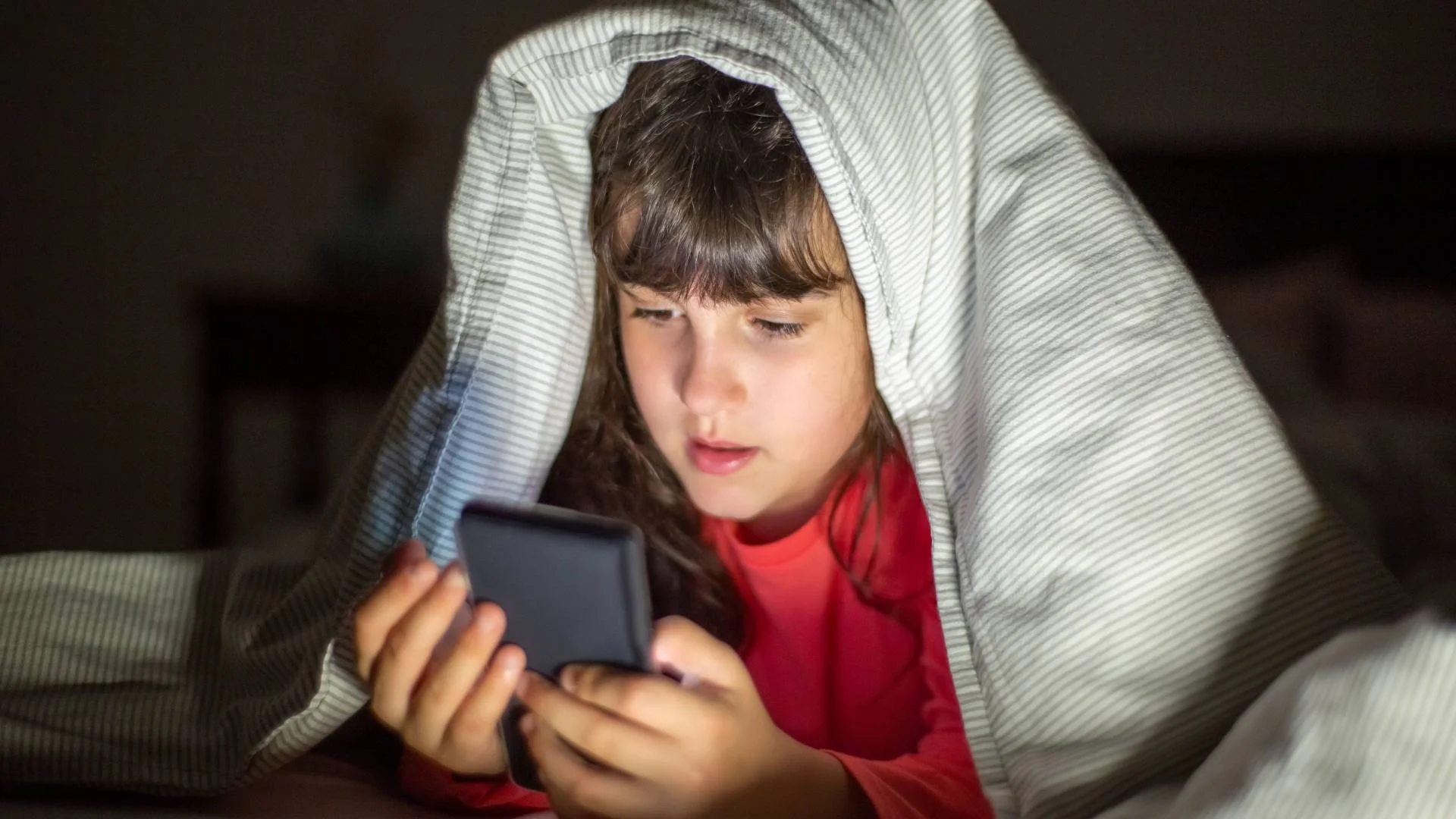 dziecko ze smartfonem pod kołdrą