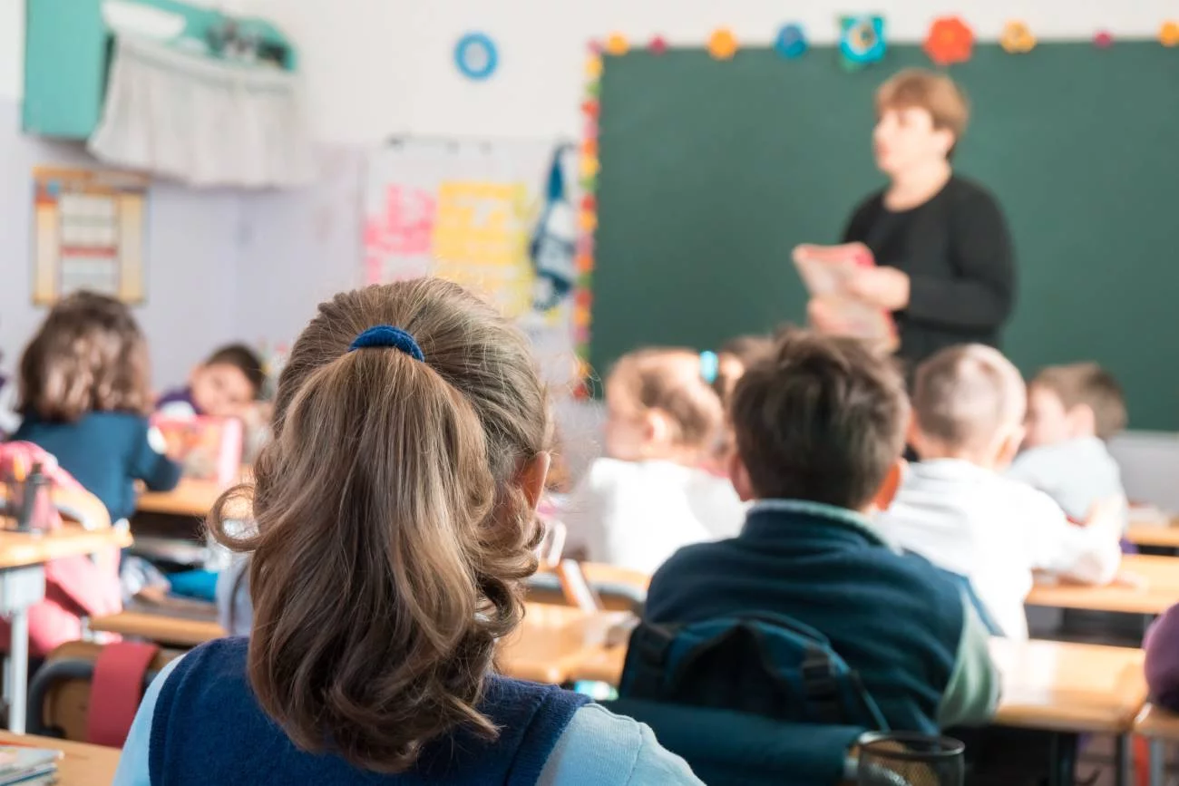 Uczniowie na lekcji siedzą w ławkach i słuchają nauczyciela.