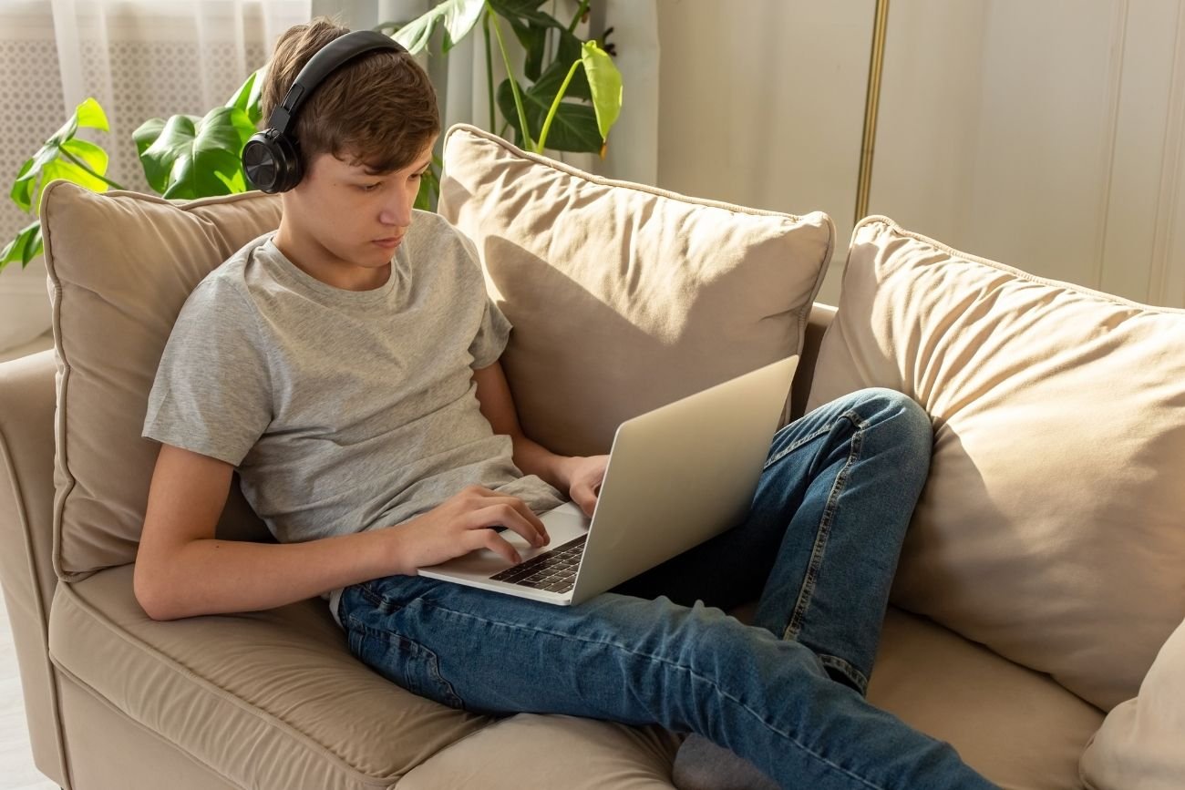 Nastolatek leży na kanapie z laptopem