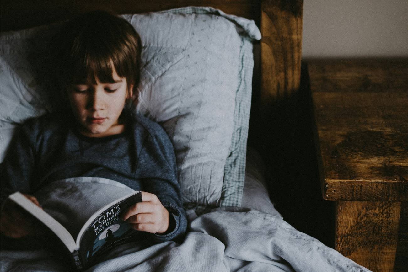 Chłopiec leży w łóżku i czyta szkolną lekturę.