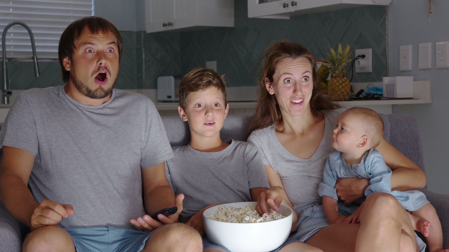 Na zdjęciu rodzina siedzi na kanapie i ogląda tv – po minach widać, że film czy bajka mogą wzbudzać strach